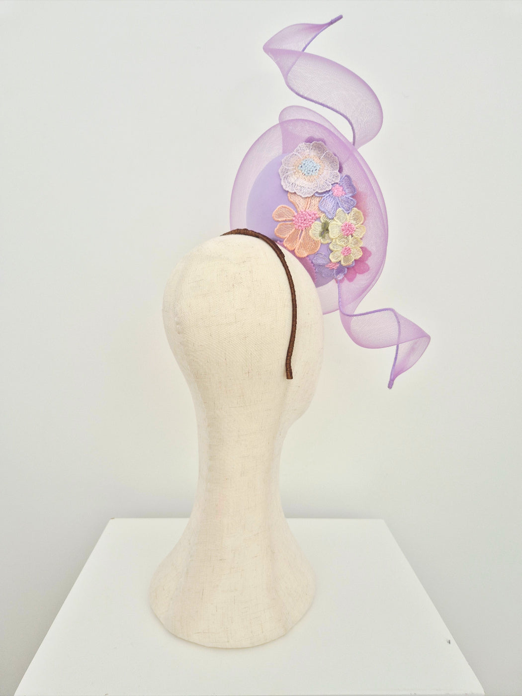 Decorative headpiece with floral lace and swirl on a mannequin head against a white background