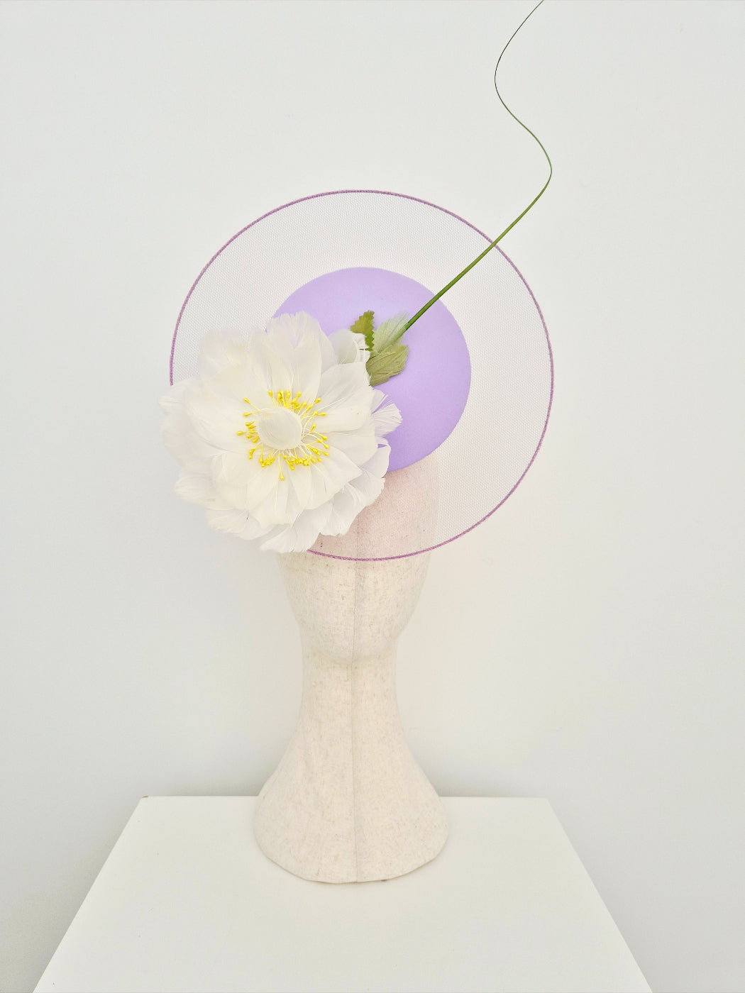 lilac satelillie percher headpiece with ivory feather flower on a mannequin head against a white wall