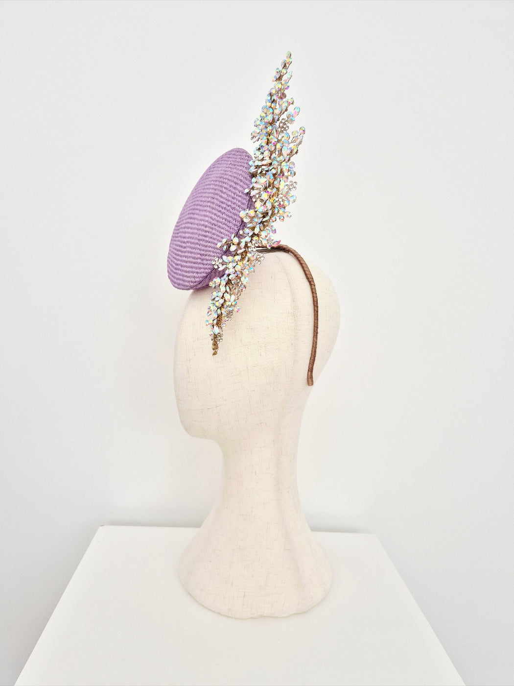 Purple headpiece with floral embellishments on a mannequin head against a white background side front