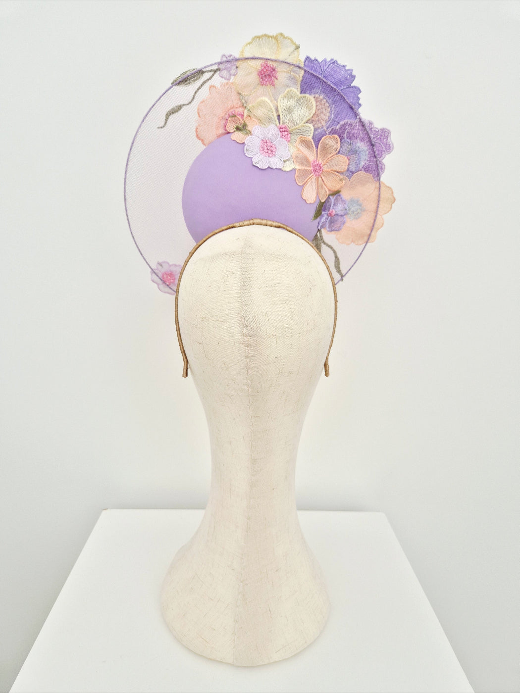 Decorative lilac headpiece with flowers on a mannequin head against a white background