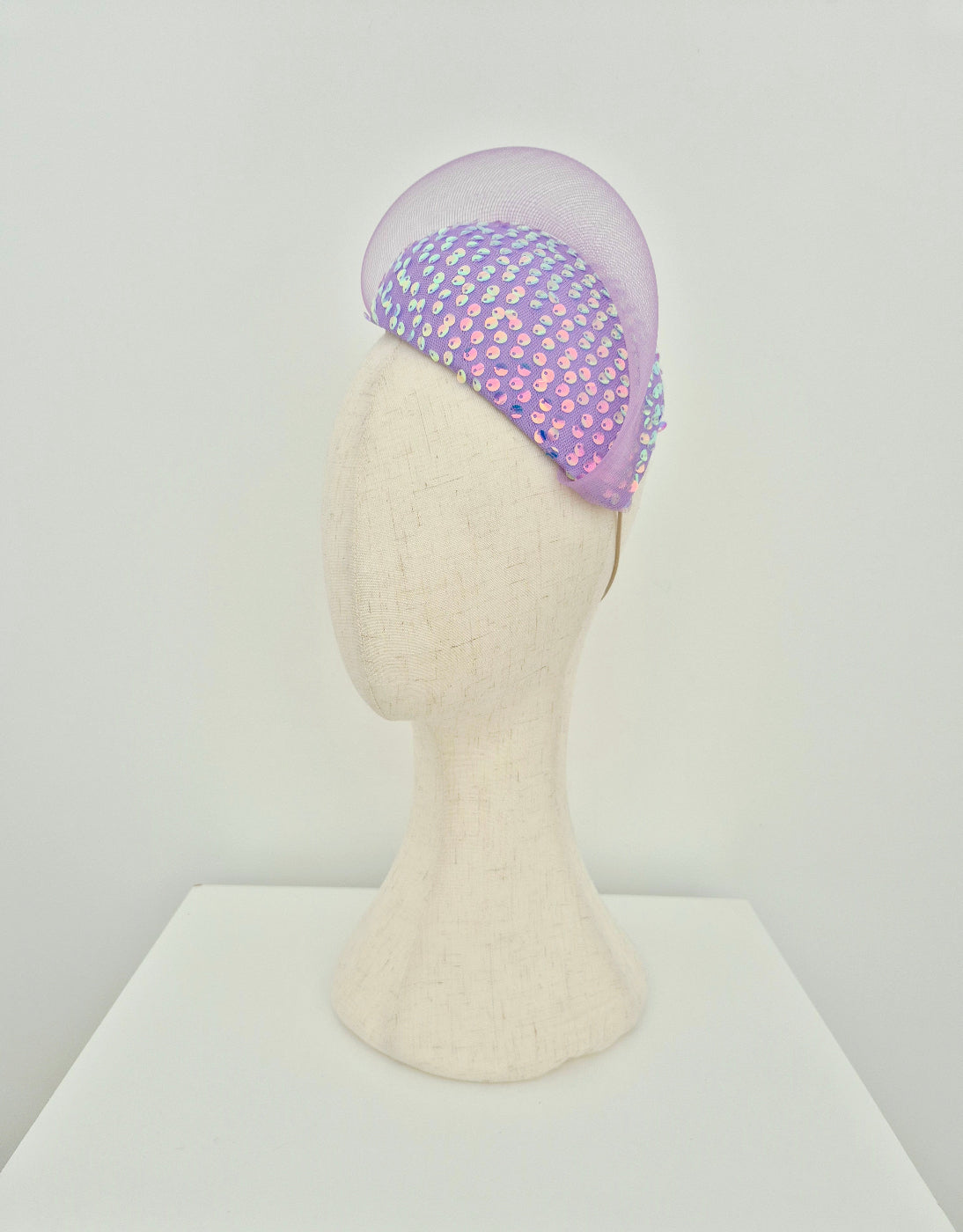 Mannequin head wearing a lilac sequin headpiece with crinoline  wave on a white background side view