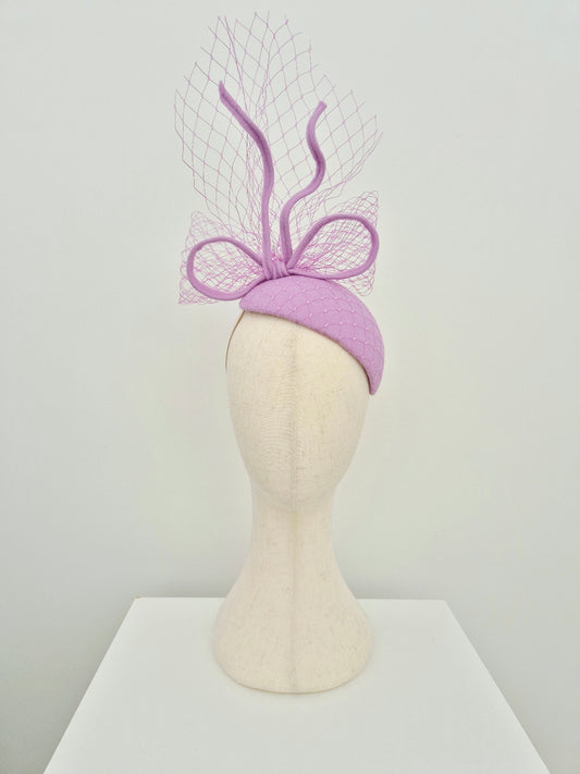 Lilac wool headpiece with decorative bow on a mannequin head against a white background