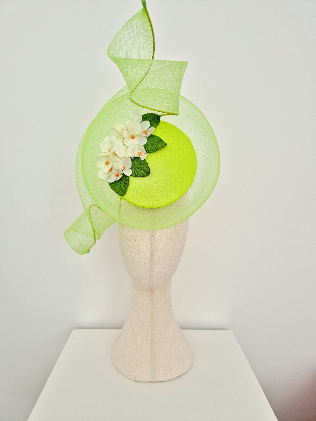 Lime green percher headpiece with flowers on a mannequin head against a white background