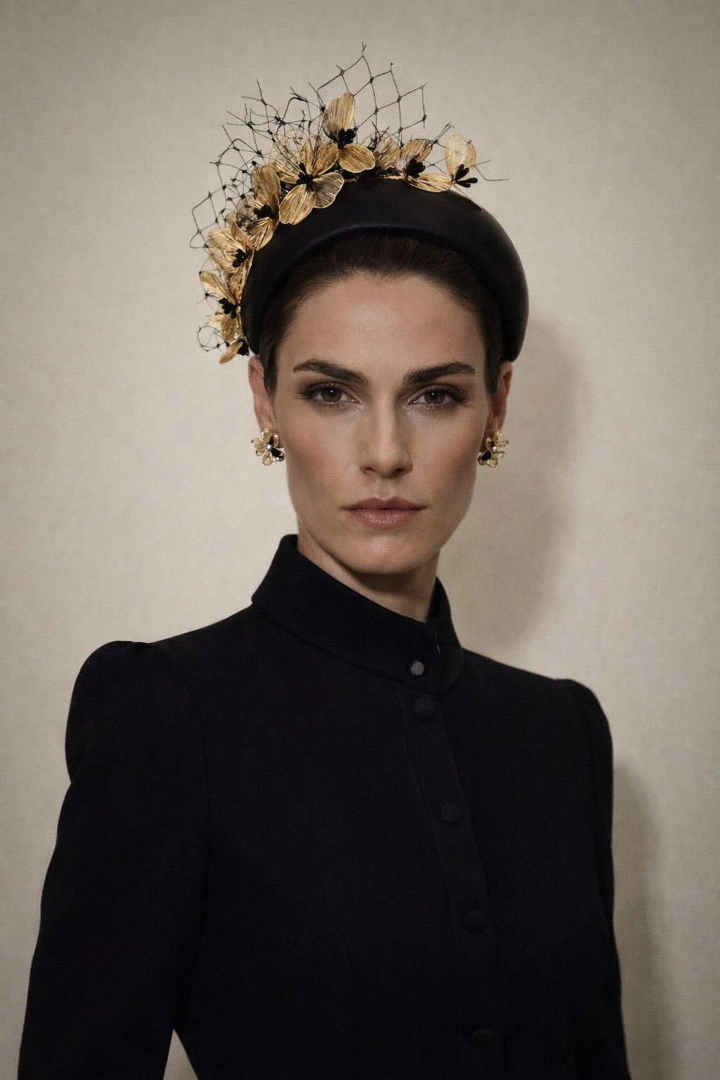Woman wearing a black coat and decorative headpiece against a plain background