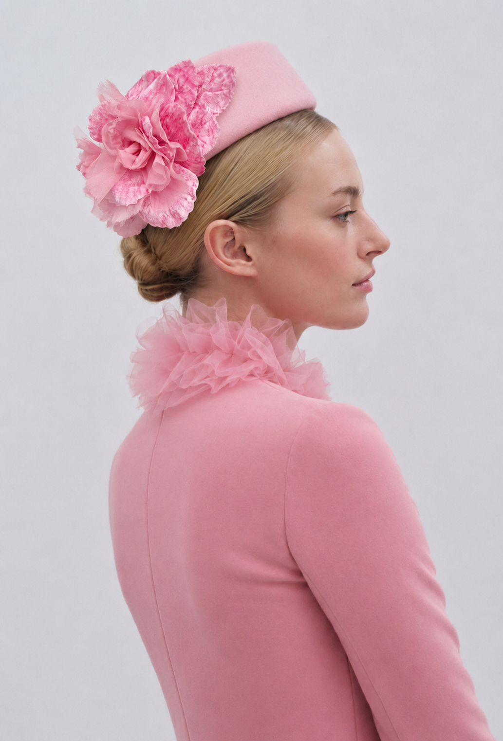 Woman wearing a pink headpiece with floral details and matching pink outfit on a light gray background