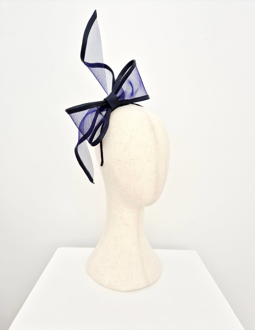Navy blue an bow headband on a mannequin head against a white background