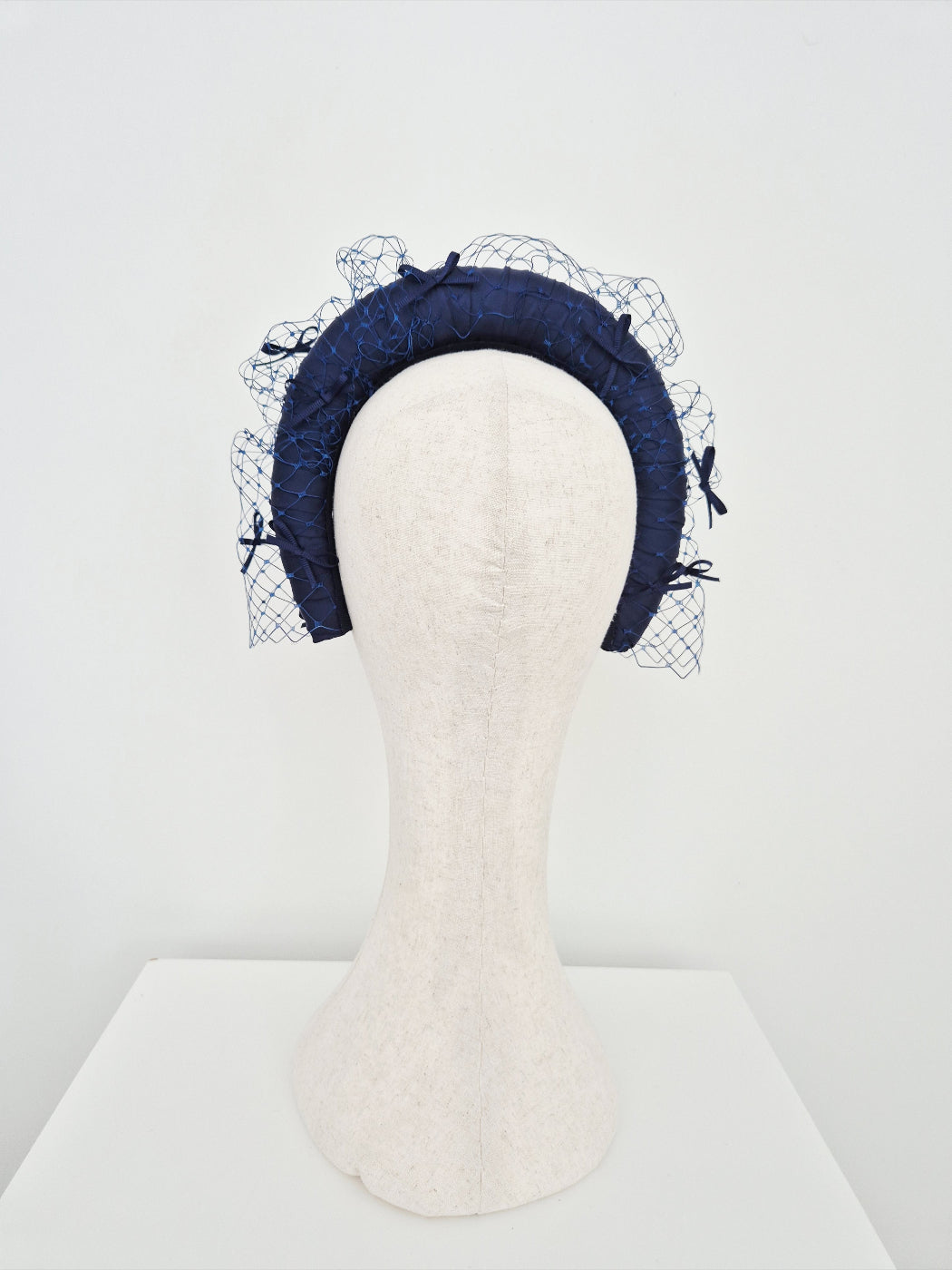 Navy blue headband with veiling details on a mannequin head against a white background back view