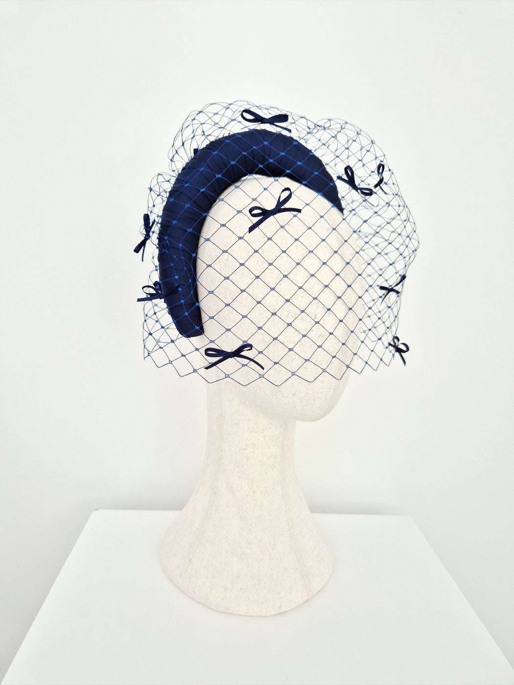 Navy blue headband with veiling and bow details on a mannequin head against a white background side front