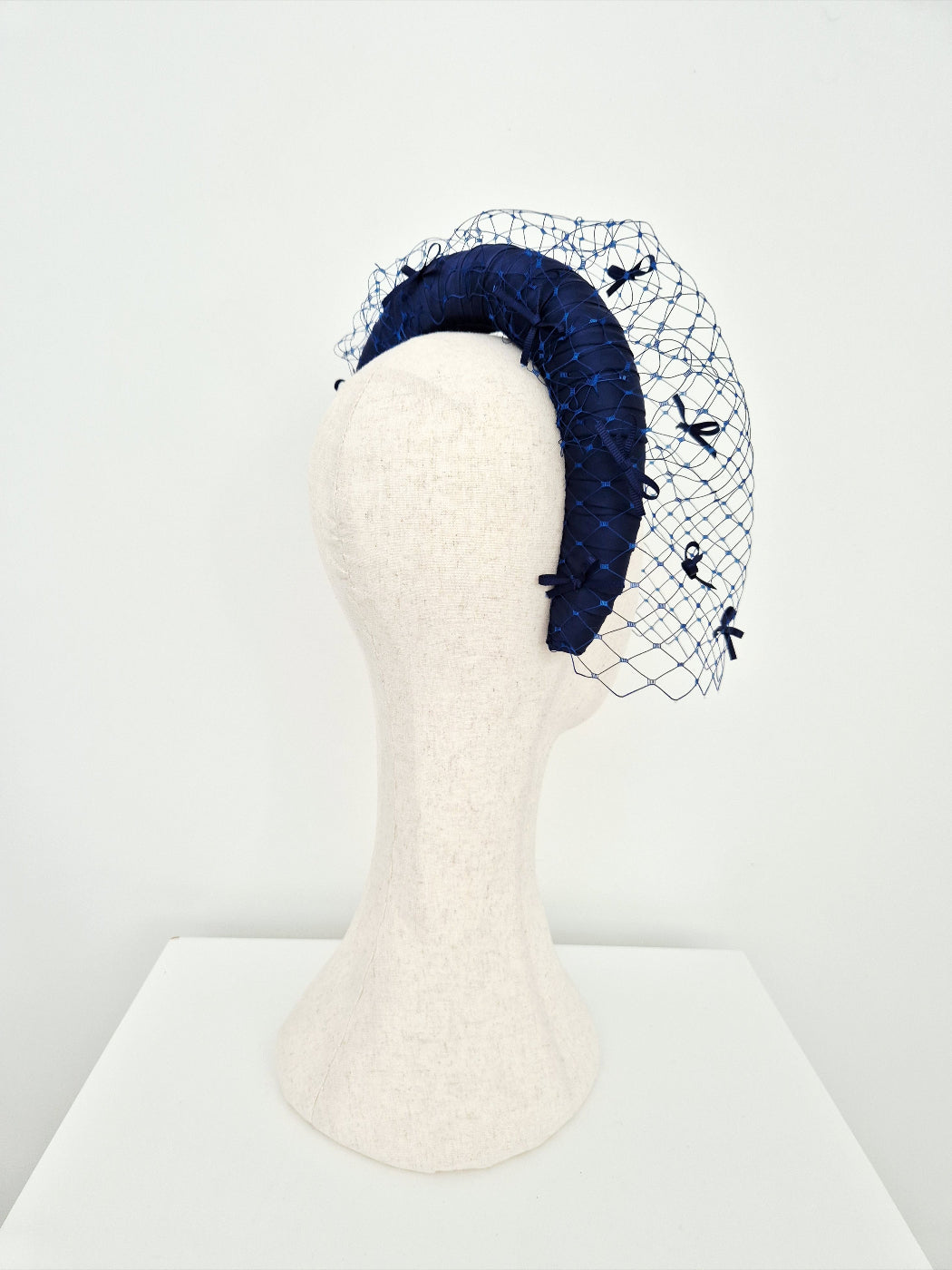 Navy blue headband with a decorative veil on a mannequin head against a white background side view