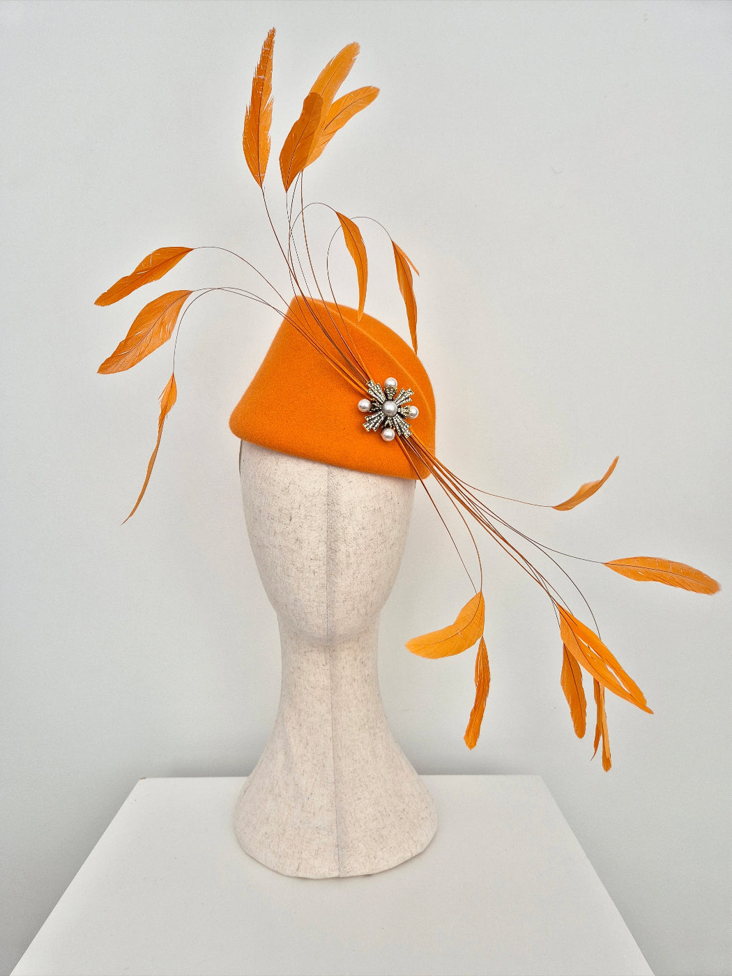 orange wool felt headpiece with feathers on a manniquin head against a white background