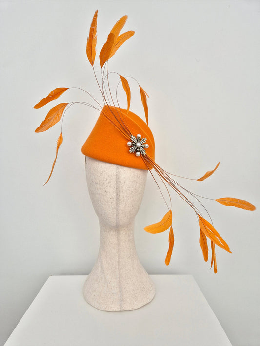 orange wool felt headpiece with feathers on a manniquin head against a white background
