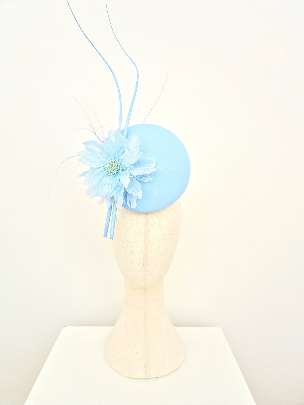 Light blue fascinator with a flower on a mannequin head against a white background