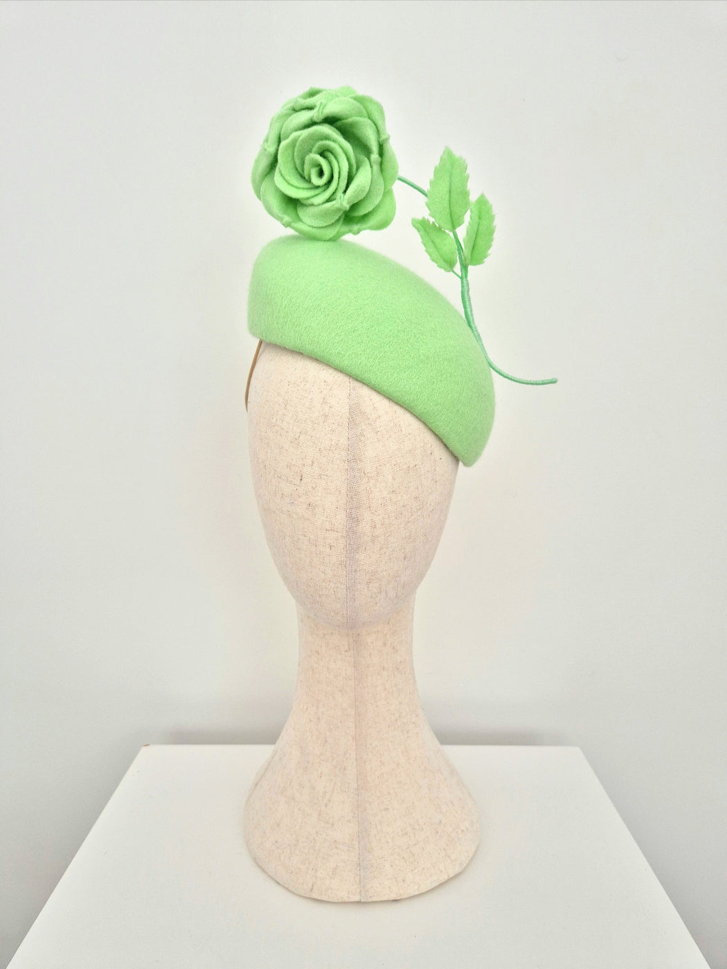 mint green hat with floral decorations on a mannequin head against a white background