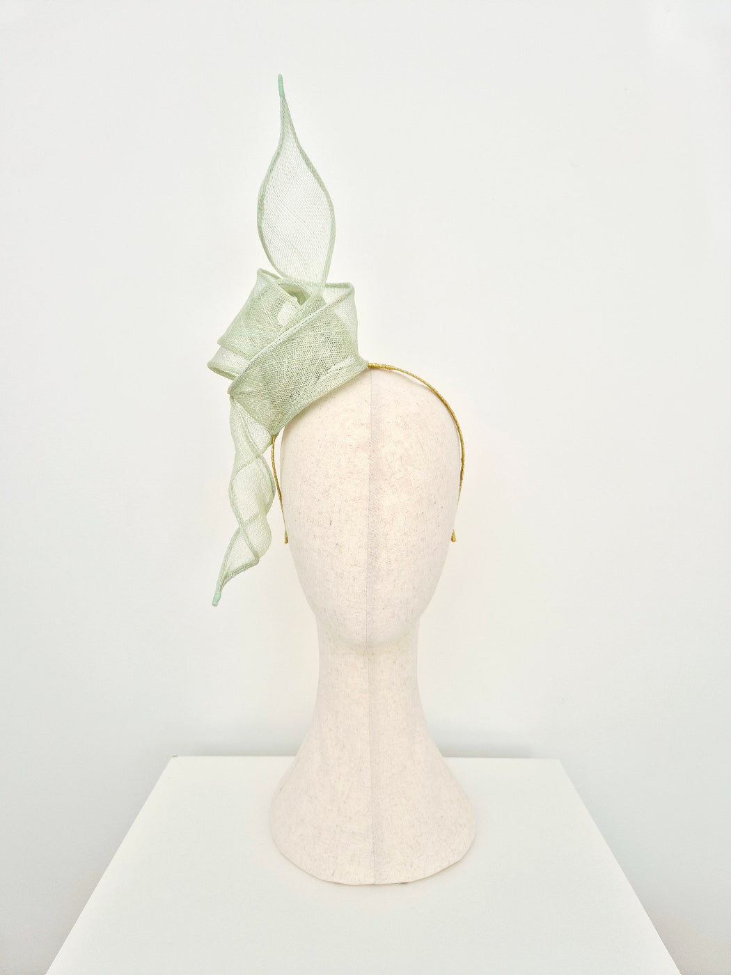 pale mint green fascinator made from straw on a headband on a manniquin head against a white background