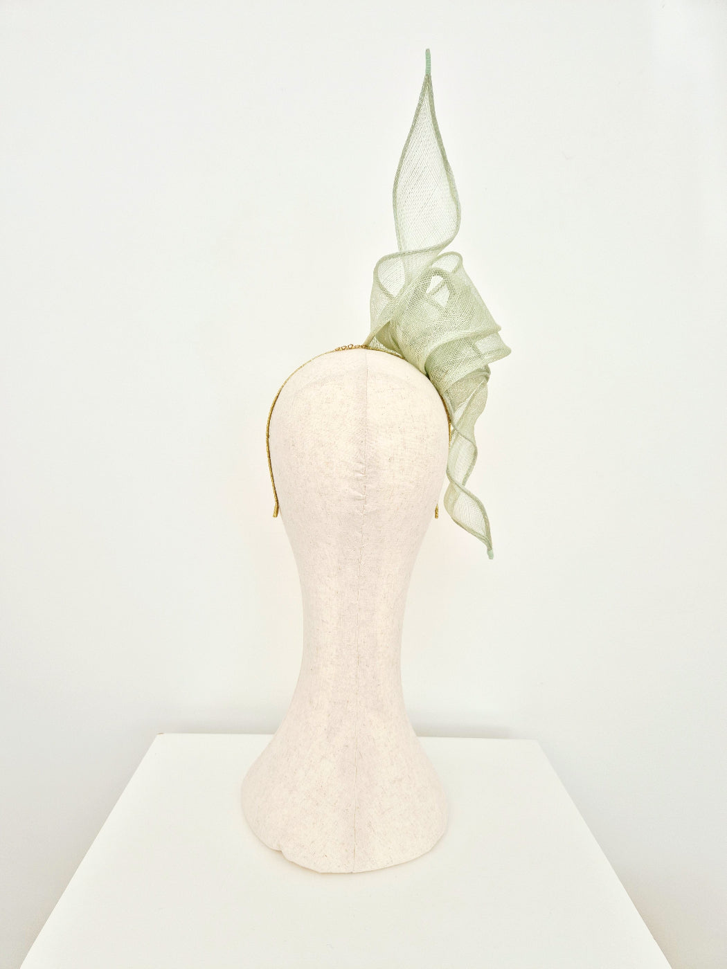 mint green straw knot and tail headband fascinator on a manniquin head against a white background back view