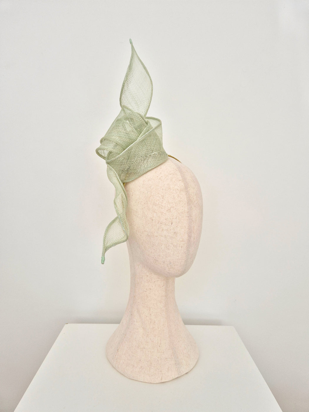 pale mint green straw fascinator on a manniquin head against a white background side view
