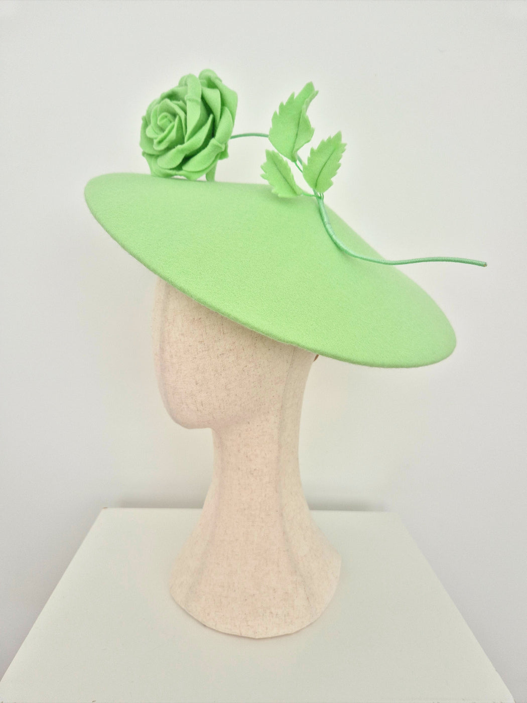 Green fascinator hat on a mannequin head against a white background side view