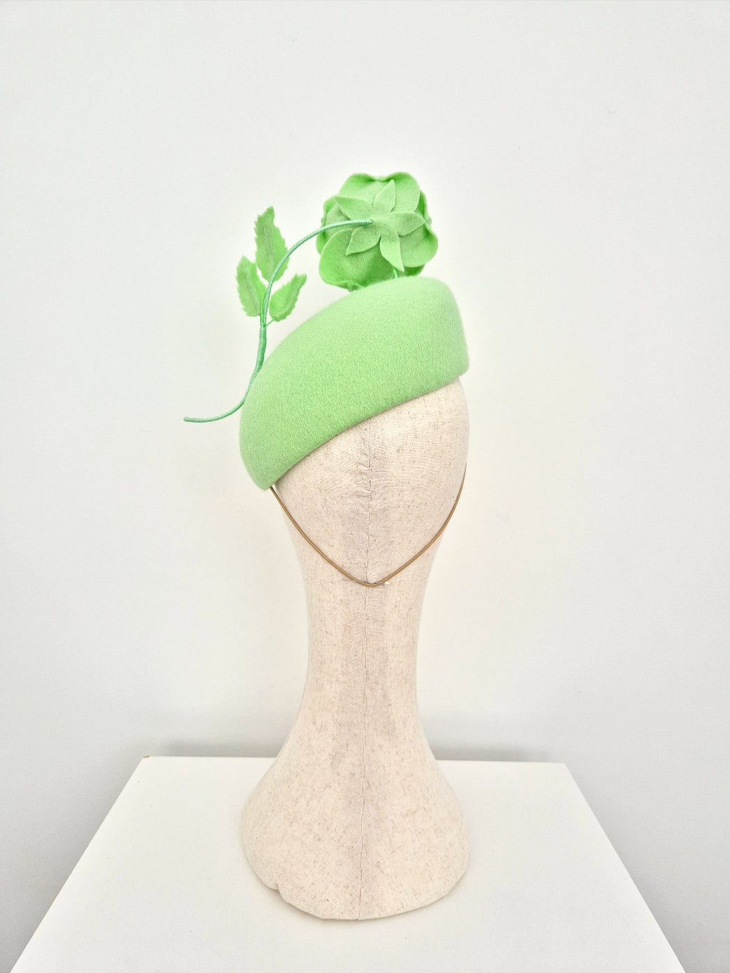 Mannequin head wearing a light green hat with a rose on a white background back view