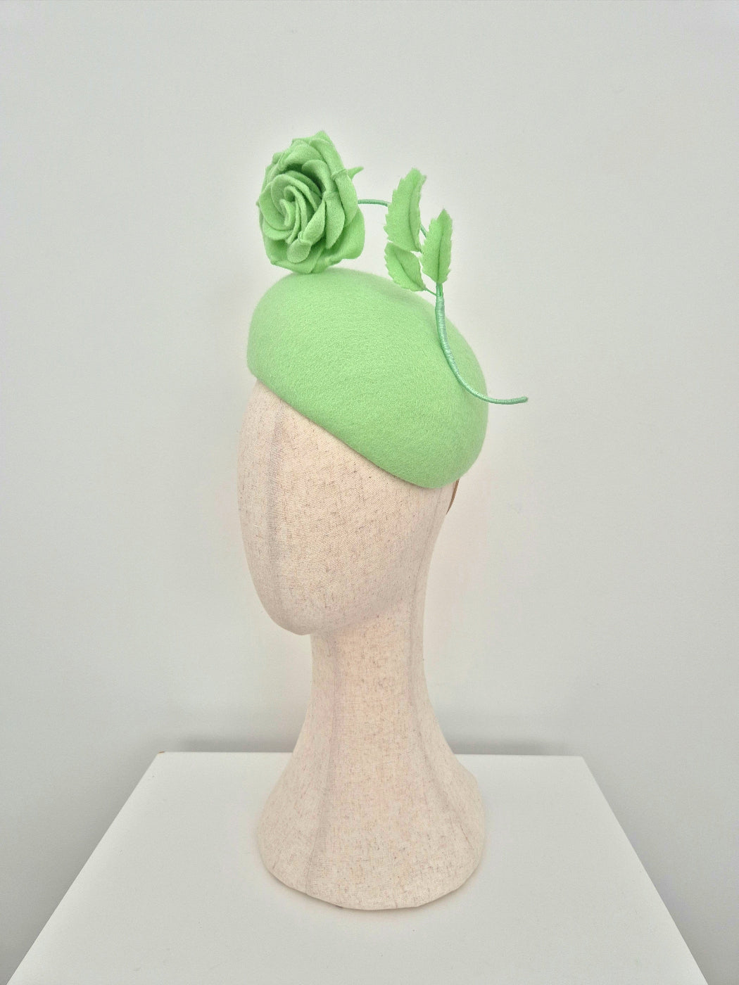 Green headpiece with floral details on a mannequin head against a plain background side view