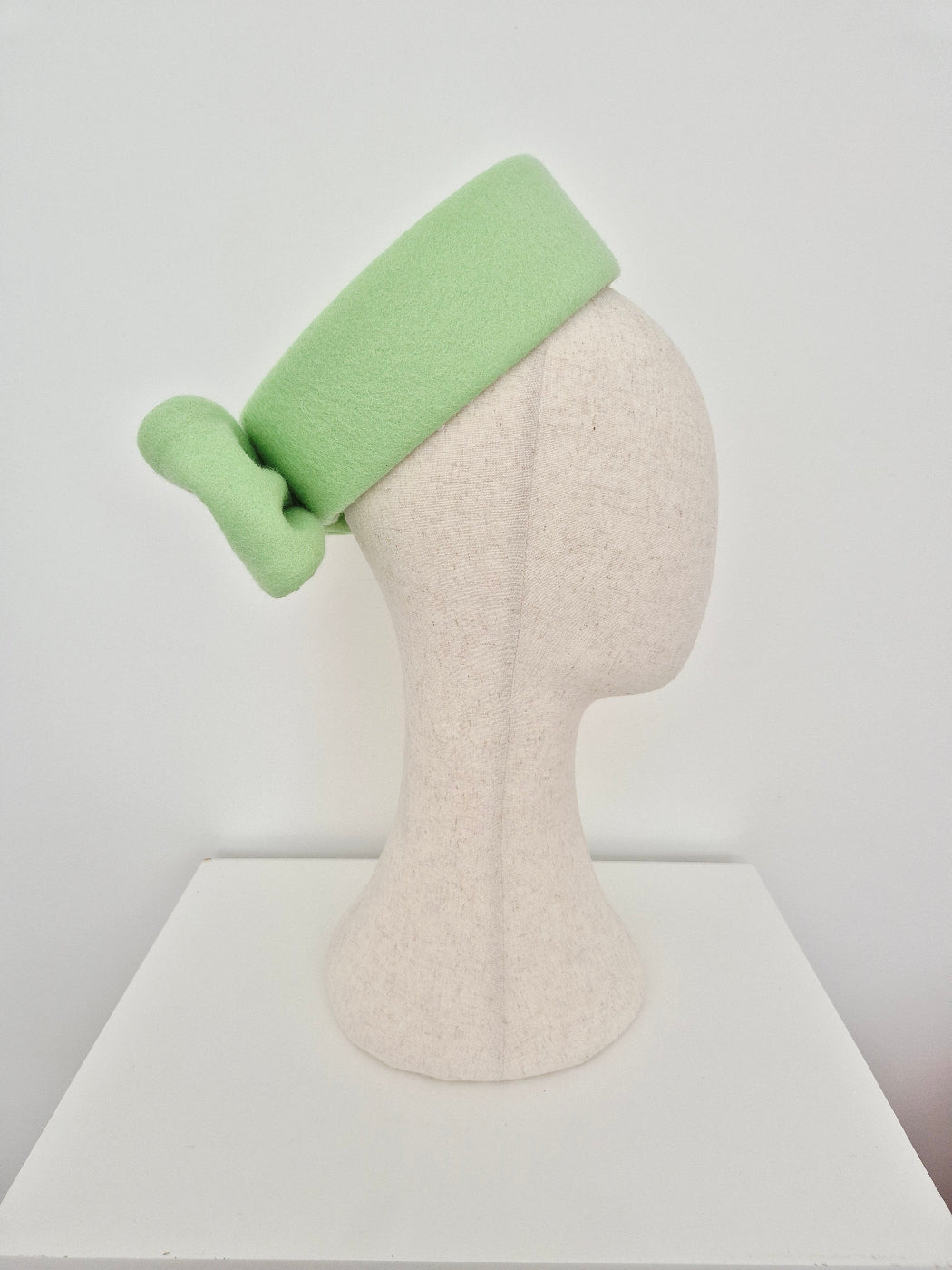 pale mint green pillbox fascinator on a manniquin head against a white background side view