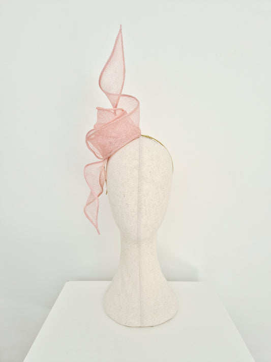 A pale pink straw fascinator on a mannequin head, set against a clean white background.