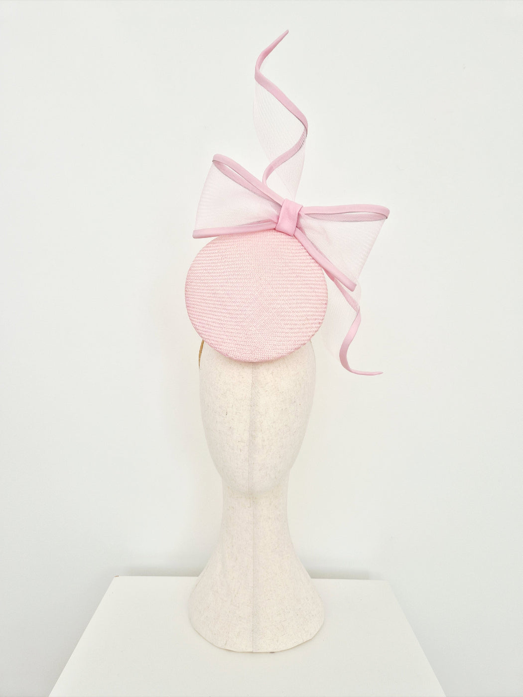 A light pink percher straw fascinator with a large bow  on a mannequin head against a plain white background.