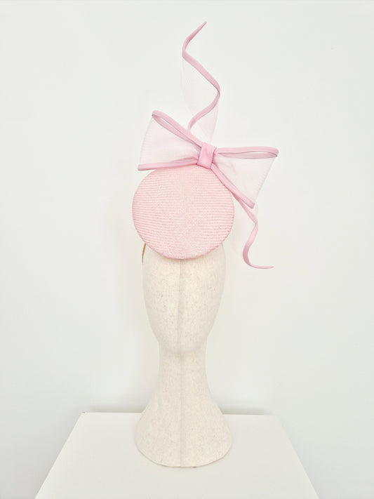 A light pink percher straw fascinator with a large bow  on a mannequin head against a plain white background.