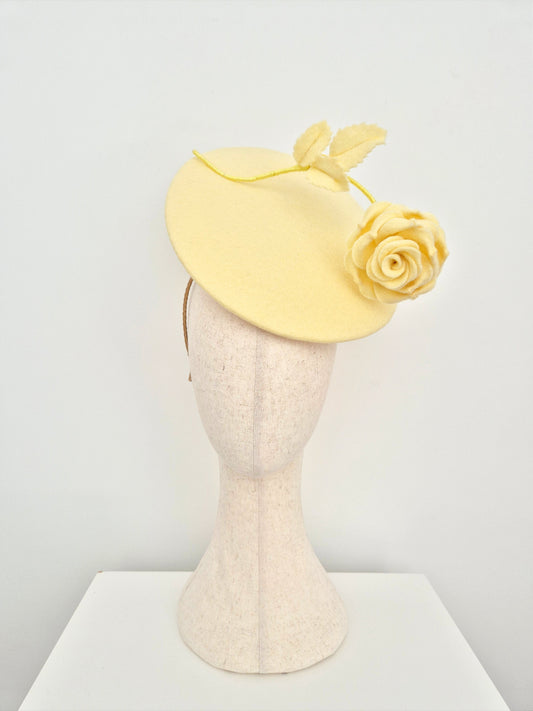 Yellow fascinator with a rose on a mannequin head against a white background