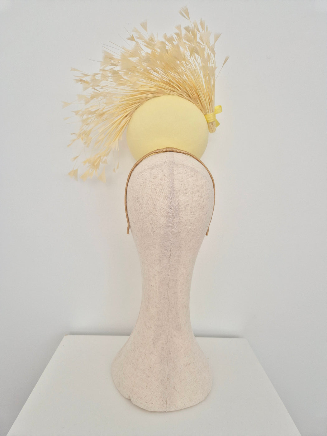 Yellow headpiece with feathers on a mannequin head against a white background back view