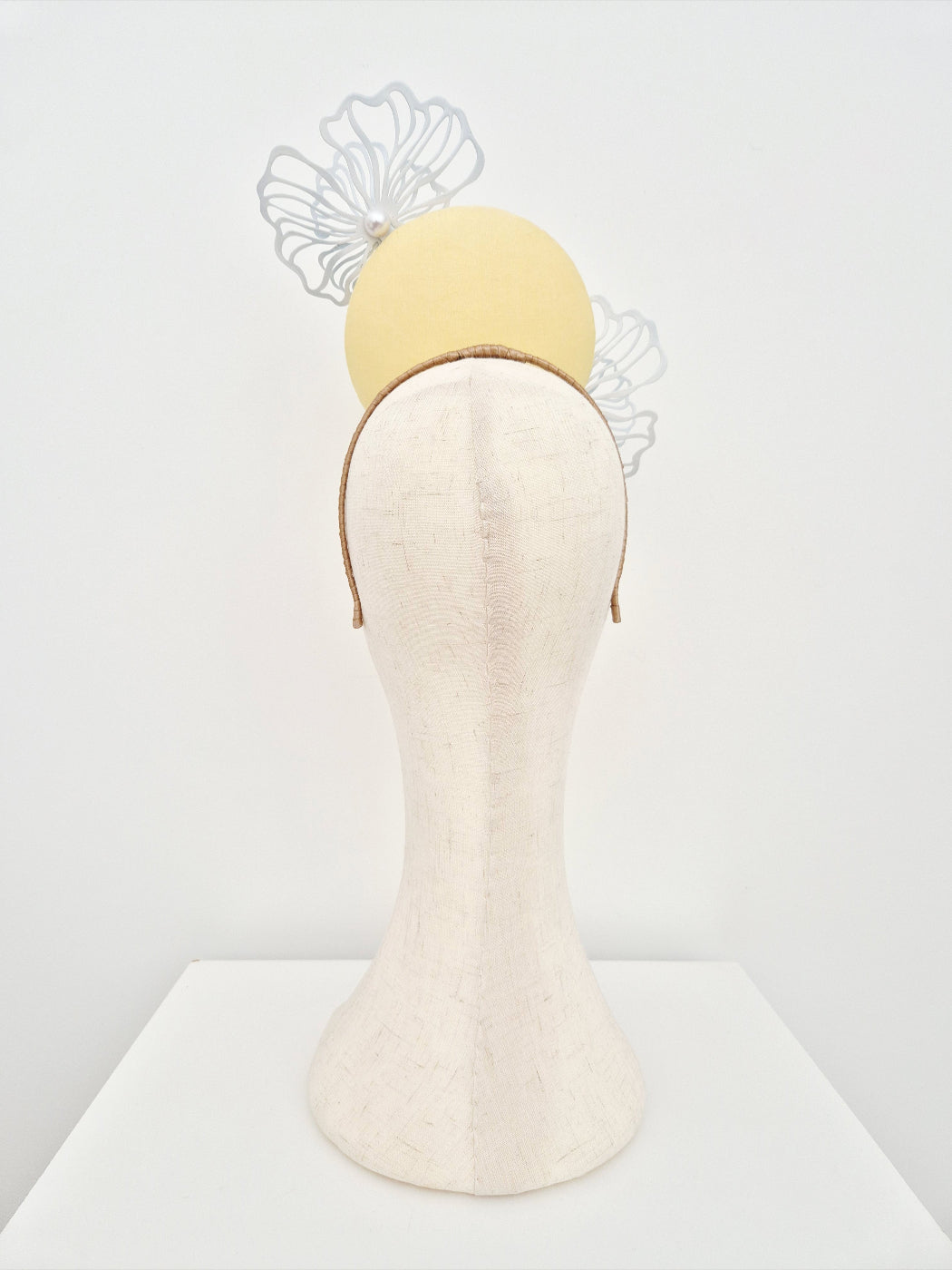 Yellow headband with decorative flower elements on a mannequin head against a white background back view