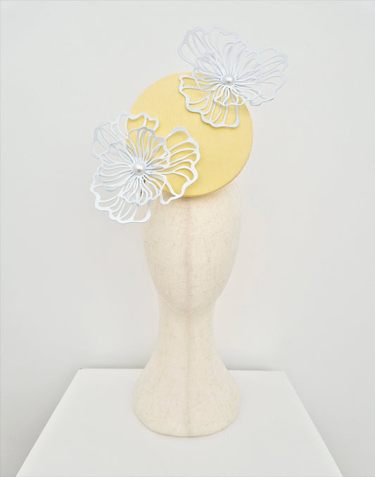 Yellow fascinator with white floral decorations on a mannequin head against a white background