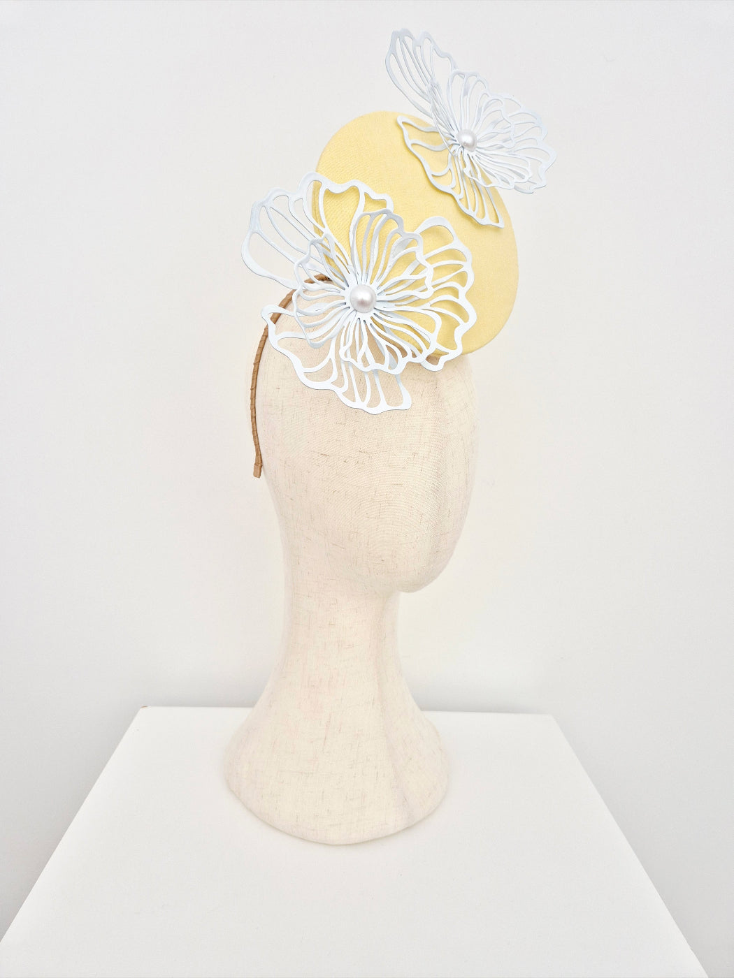 Yellow headband with white floral designs on a mannequin head against a white background side front
