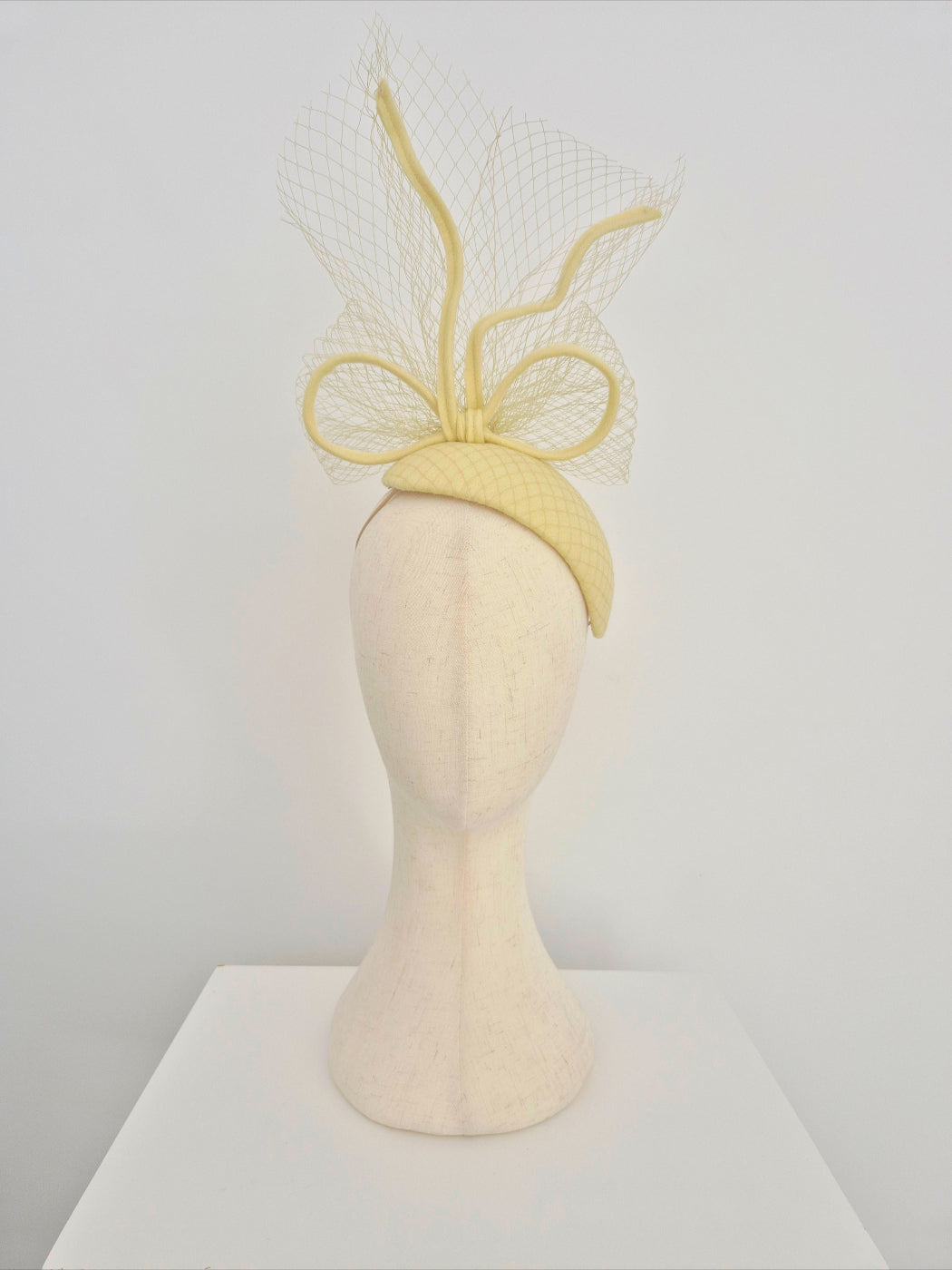 Pale Yellow headpiece with bow and veiling on a mannequin head against a white background