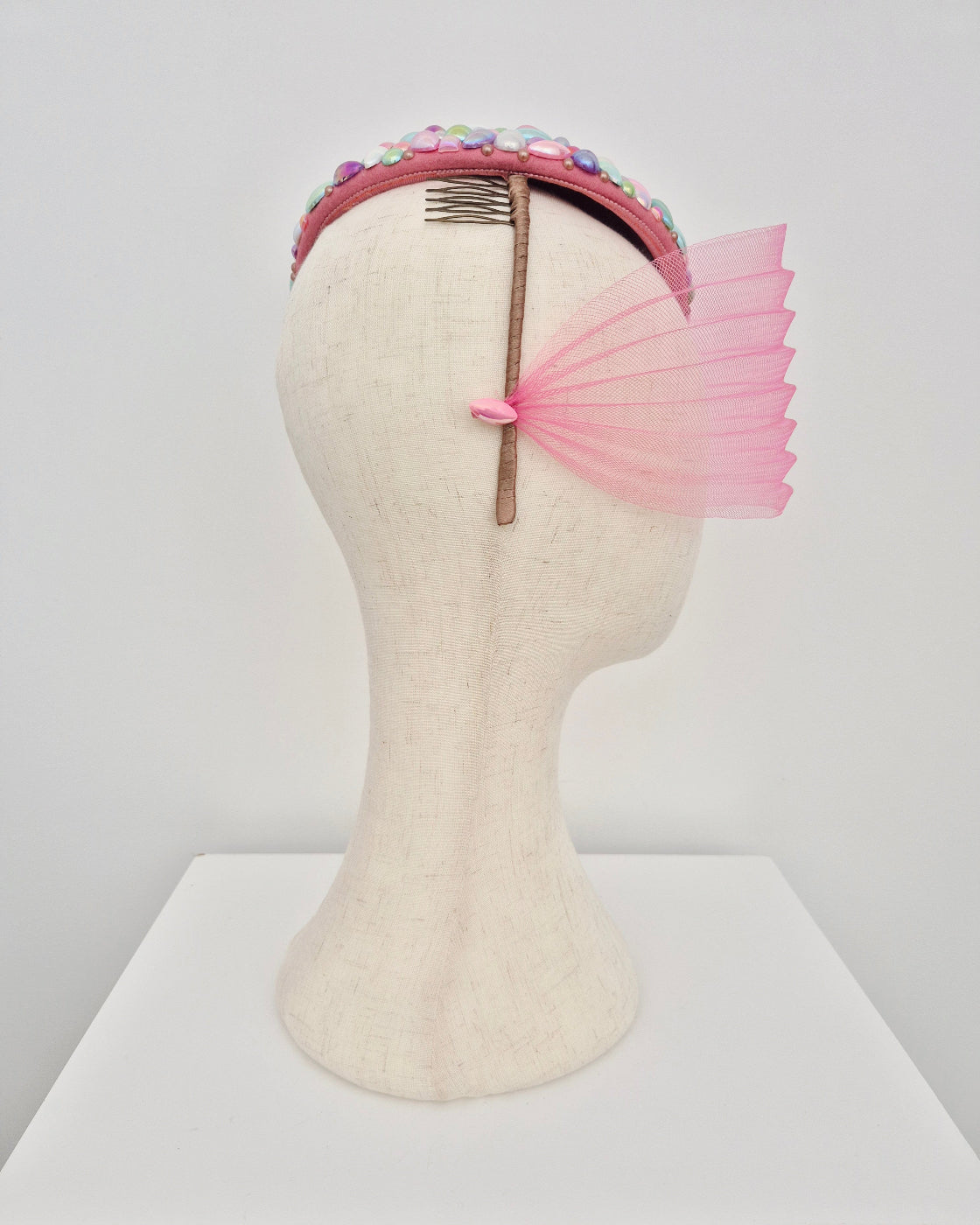 Decorative headpiece with pink face veil on a mannequin head against a white background