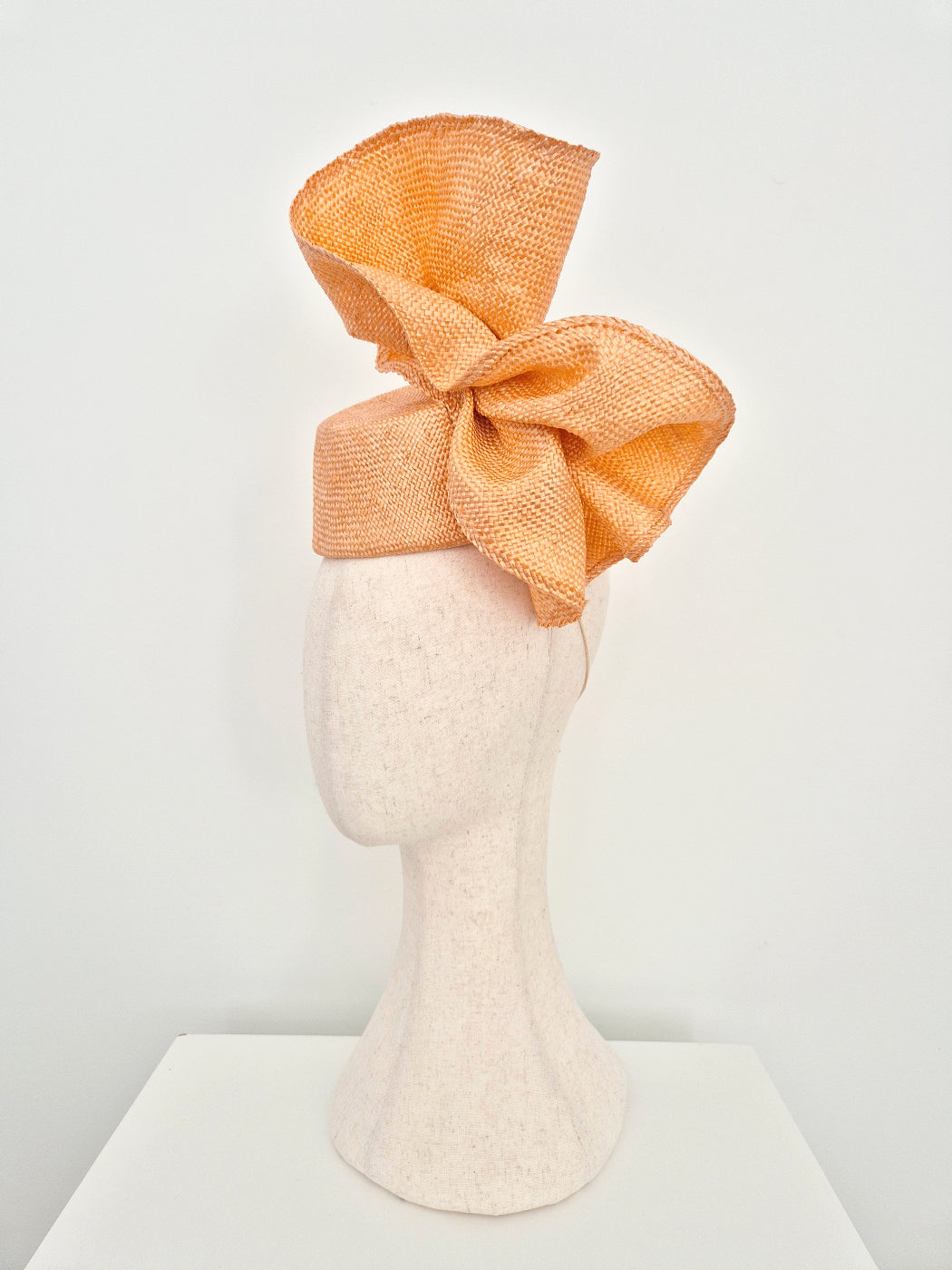 An peach straw fascinator with a large bow, displayed on a textured off-white mannequin head against a clean white background.side view