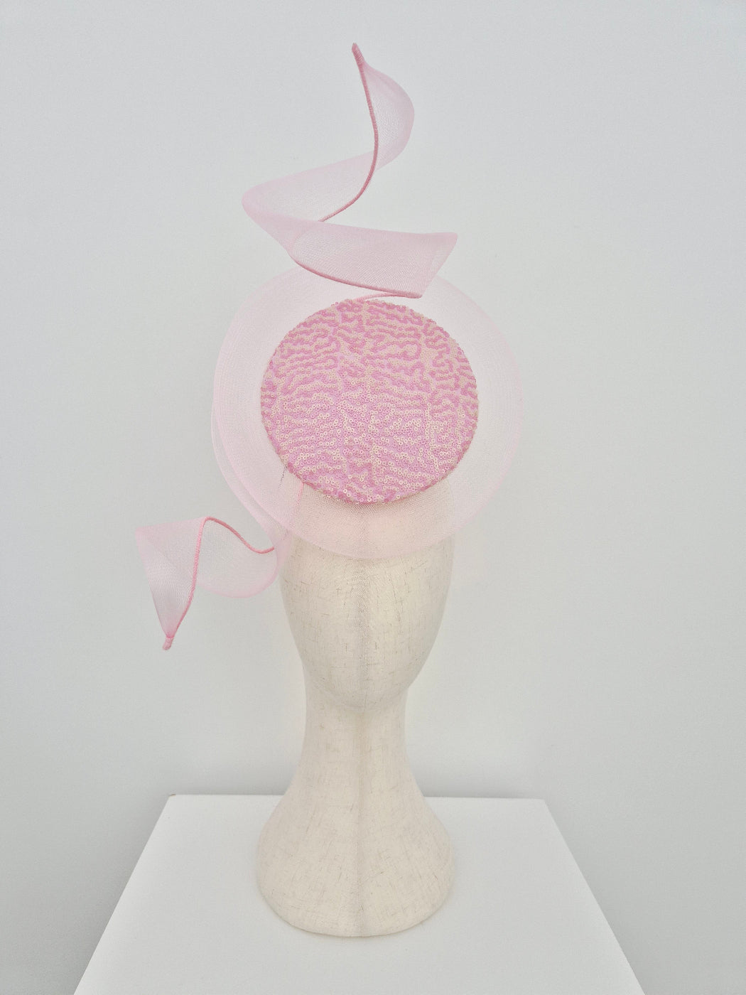 pink and cream percher headpiece with crinoline swirl on a manniquin head against a white background