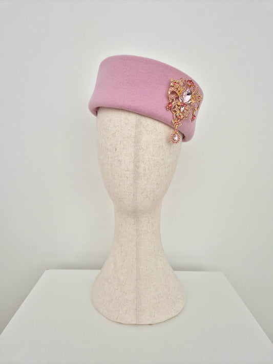 Pink pillbox headpiece with brooch on a mannequin head against a white background