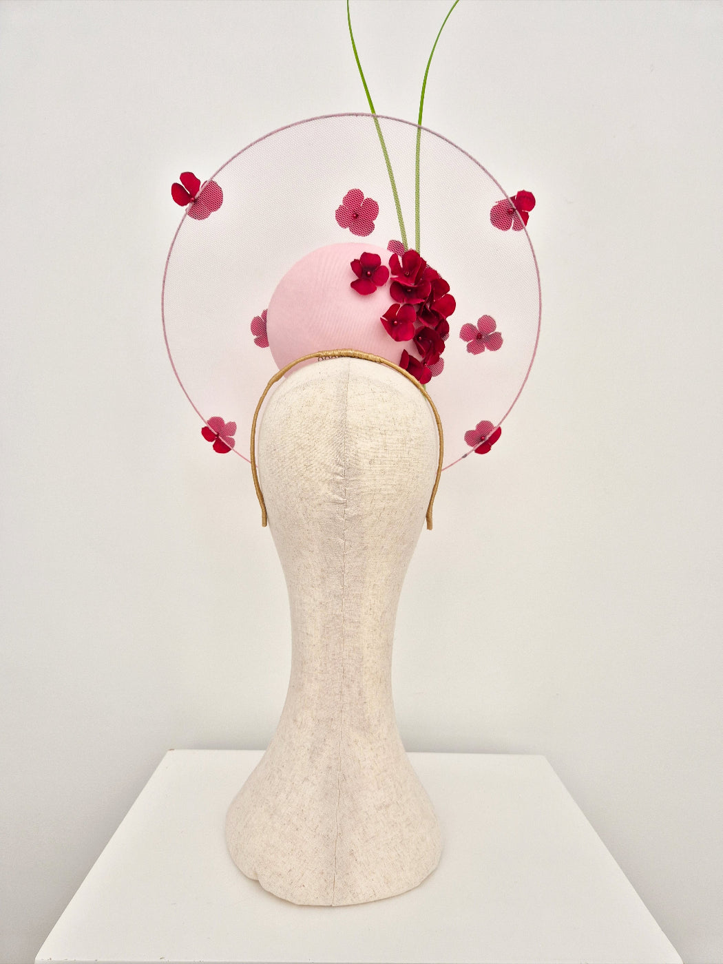 Headpiece with pink sphere and burgundy flowers on a mannequin head against a white background back view