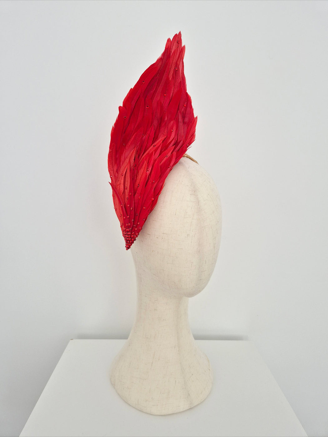 Red feathered headpiece on a mannequin head against a white background