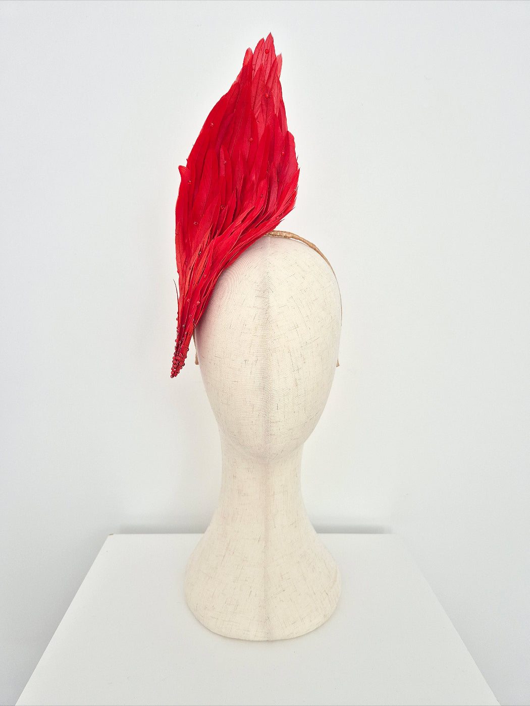 Red feathered headpiece on a mannequin head against a white background