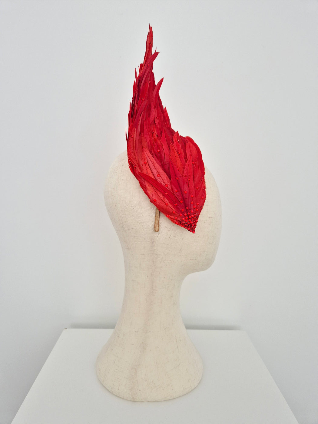 Red feathered headpiece on a mannequin head against a white background