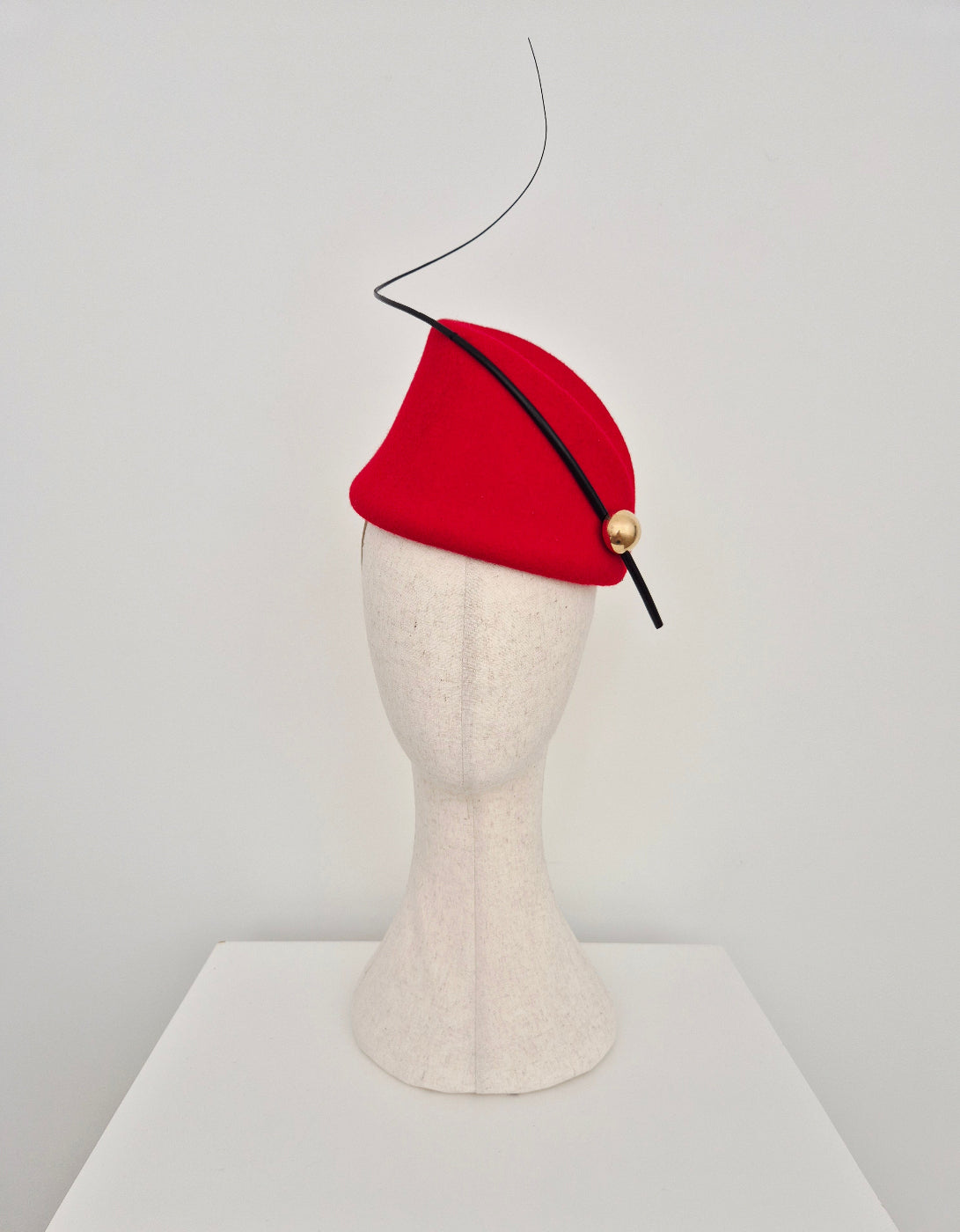 Red hat with a black quill and gold button on a mannequin head against a white background