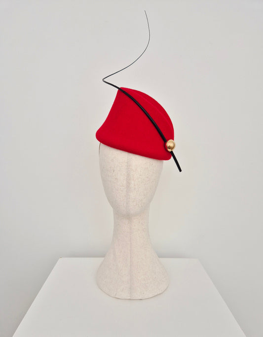Red hat with a black quill and gold button on a mannequin head against a white background