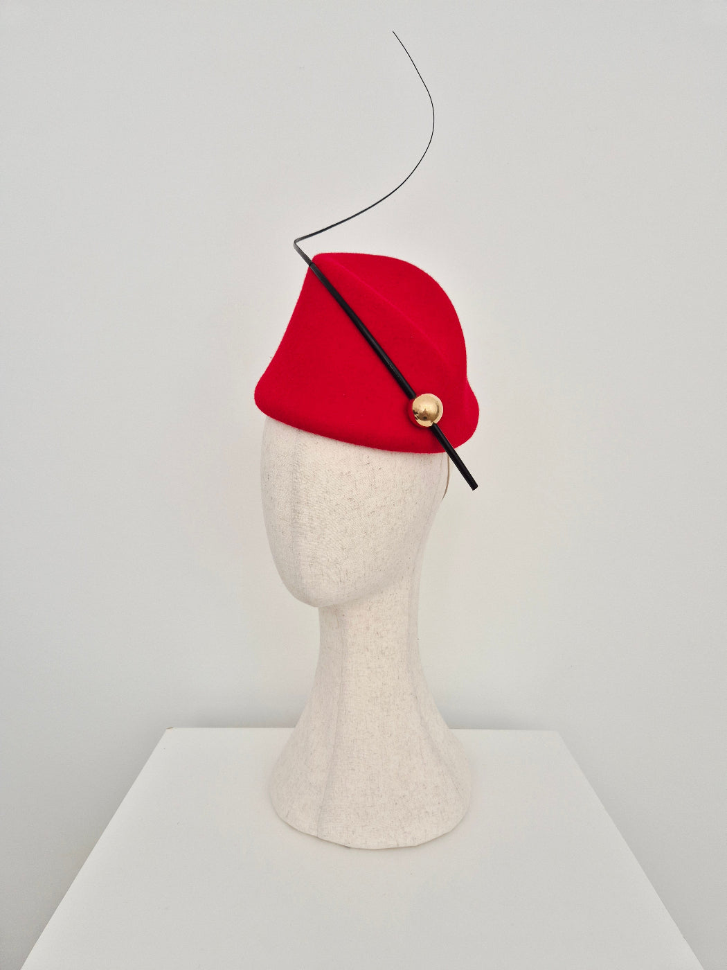  red felt topper headpiece with a black quill and a gold button on a manniquin head against white background side view