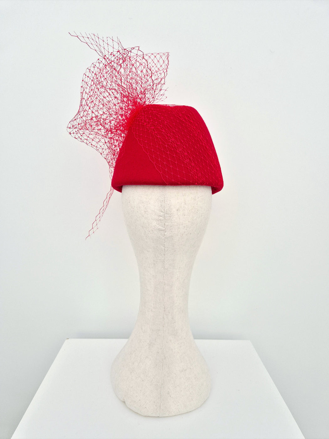 Red felt hat with a decorative net on a mannequin head against a white background back view