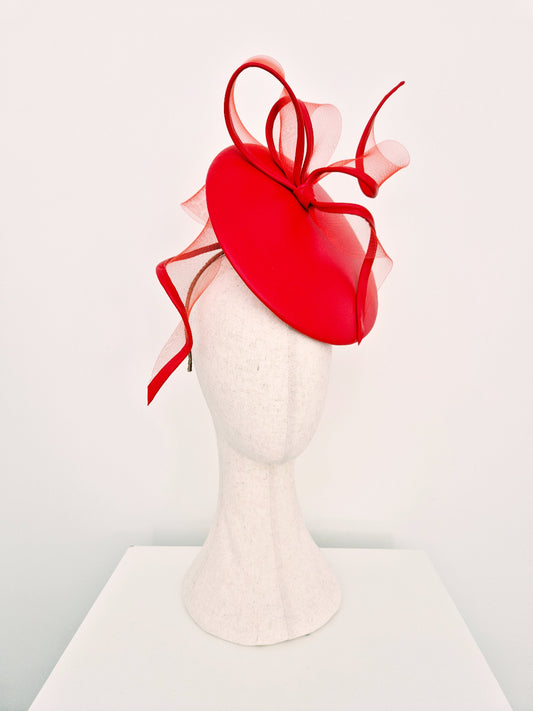 A bright red fascinator hat with matching red crinoline bow and red loops, displayed on a white mannequin head against a clean white background. side view