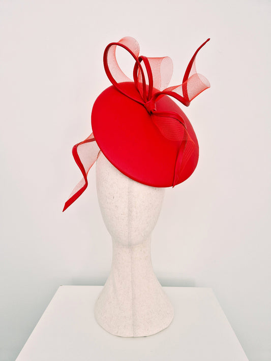 A red leather percher fascinator with red crinoline loops and bow, displayed on a white felt mannequin head against a clean white background.