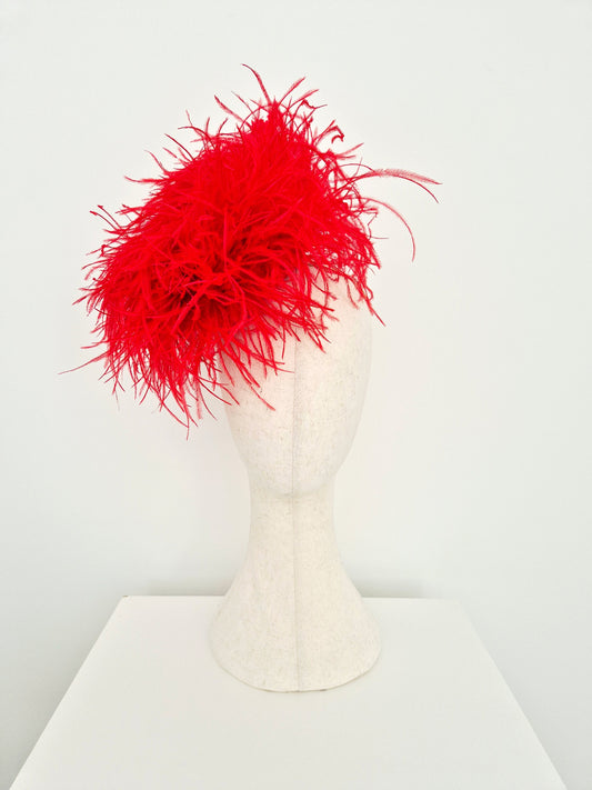 A bright red feather fascinator hat displayed on a white felt mannequin head, set against a clean white background.