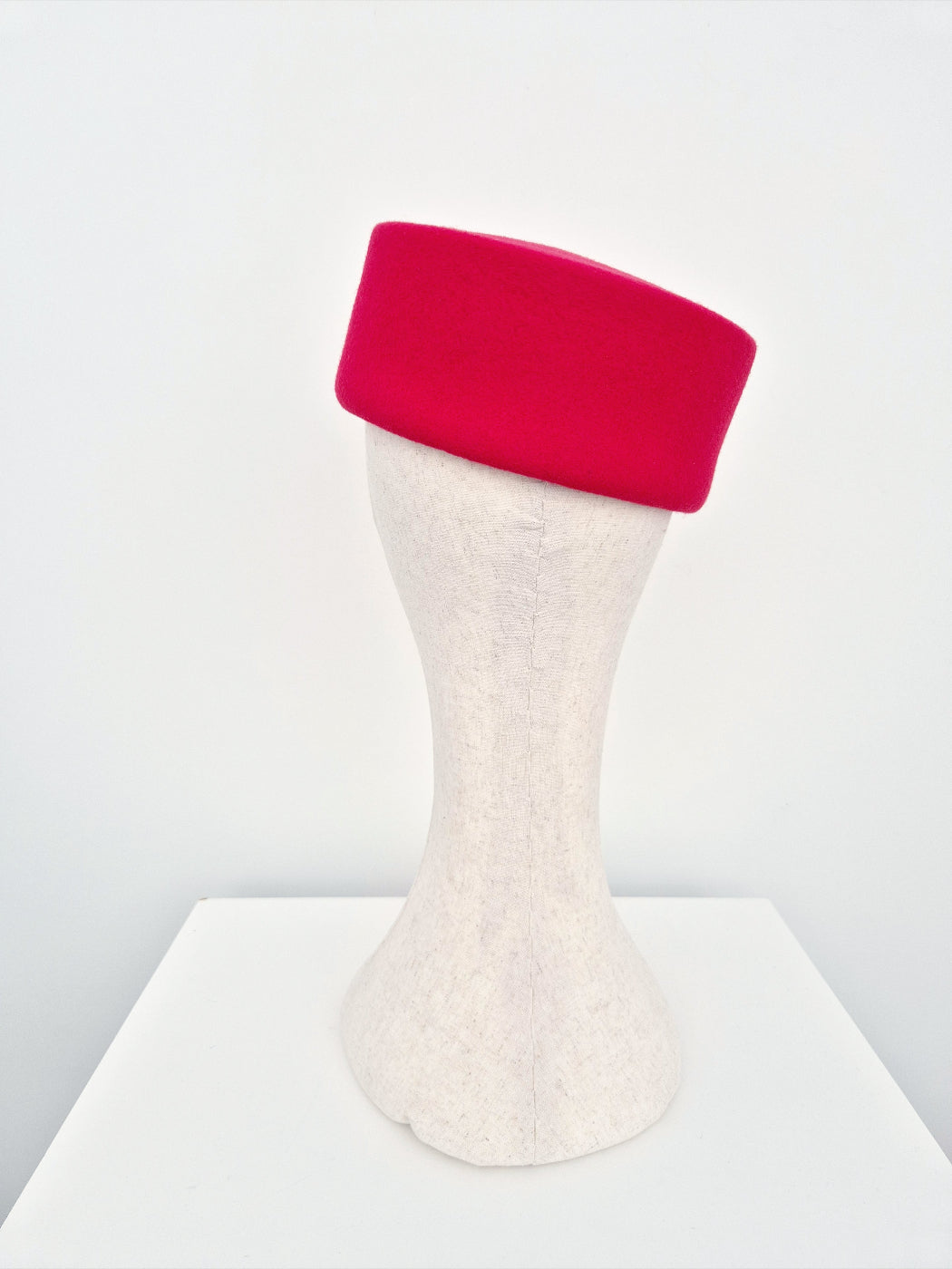 Red pillbox headpiece on a white mannequin head against a light gray background back view