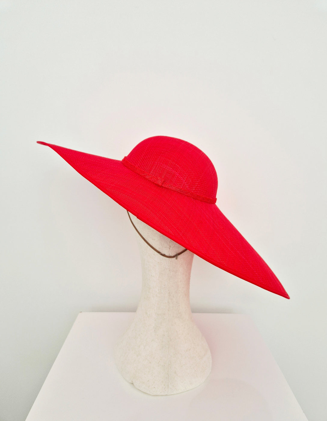 A bright red wide-brimmed straw hat displayed on a white mannequin head stand against a plain white background.back view